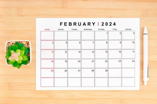 February 2024 calendar page and houseplant on wooden background with empty space.