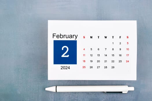 February Calendar 2024 page with pen on blue wooden background.