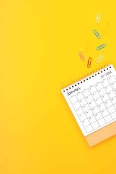 January 2024 desk calendar and paper clips on yellow color background. Position with copy space.