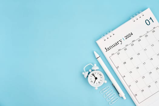 January 2024, Monthly desk calendar for 2024 year and alarm clock with paper clips on blue color background. Position with copy space.