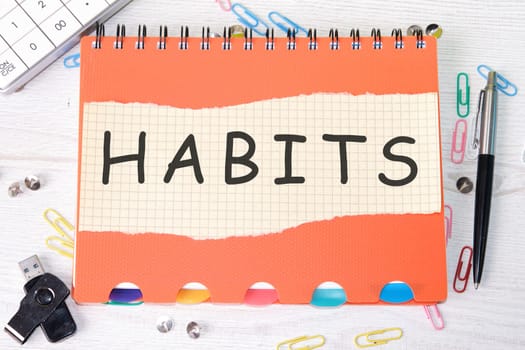 HABITS word is written on a sheet in a cage lying on a notebook on the table next to stationery