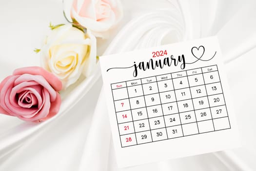 January 2024 calendar page and rose flower on white satin textile background.