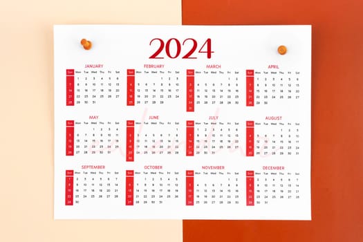 12 months calendar page for 2024 year and wooden pins on red background.