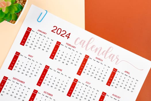 The 12 months desk calendar 2024 and paper clips on red background.