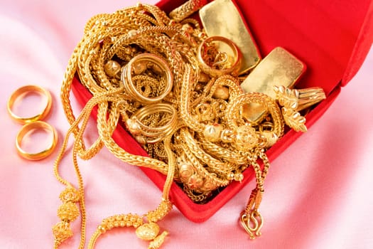 Many gold necklaces and gold bars in red box on velvet cloth background.