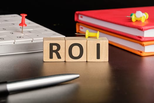 Return on investment concept. ROI the text of non-wooden cubes next to notepads, a calculator, a pen on a black background