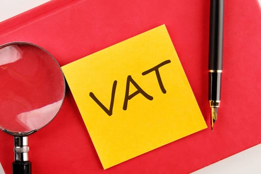 VAT the inscription on the sticker lying on a red notebook next to a magnifying glass and a fountain pen
