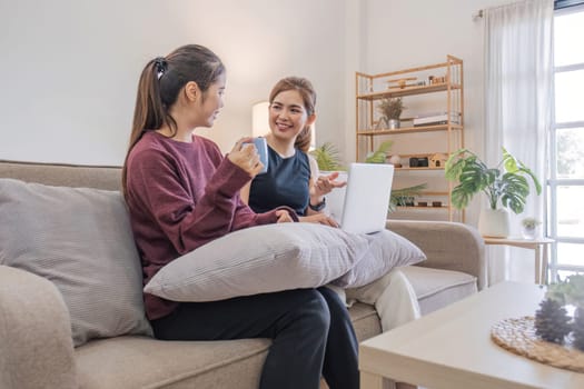 Two women communicate with friends and classmates via video link using laptop and smartphone in living room. Friends, friendship, time together..