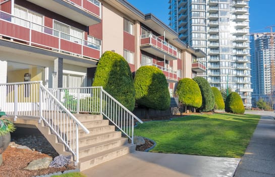 Small porch with steps to the entrance at low rise residential building on the high rise background