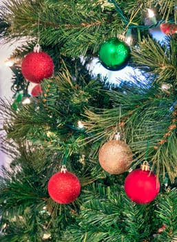 Red, golden, and green bauble on pine tree brenches. Christmas decorations on artificial tree