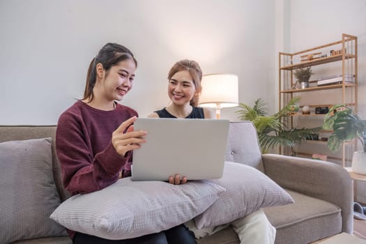 Two women communicate with friends and classmates via video link using laptop and smartphone in living room. Friends, friendship, time together..