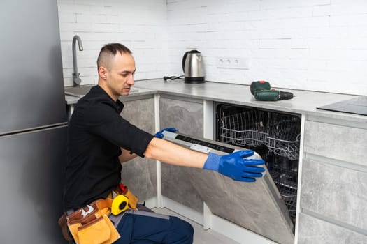Young Repairman Fixing Dishwasher With Screwdriver In Kitchen. High quality photo