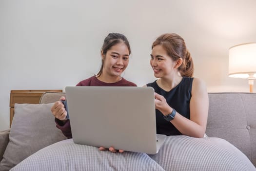 Two women communicate with friends and classmates via video link using laptop and smartphone in living room. Friends, friendship, time together..