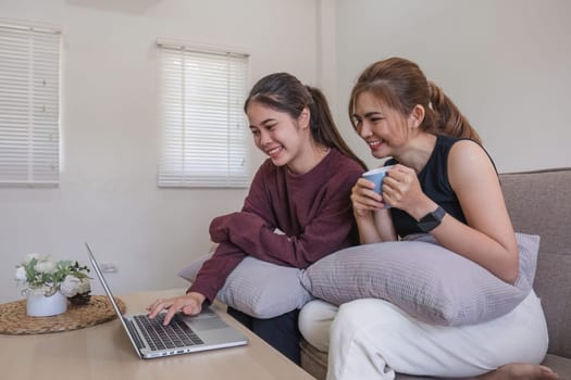 Two women communicate with friends and classmates via video link using laptop and smartphone in living room. Friends, friendship, time together..