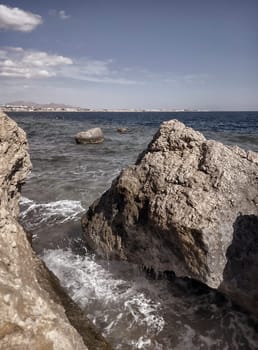 Seascape with a view of the rocky coast, beautiful sea surface, waves crashing on a rocky cliff. A clear sunny day.