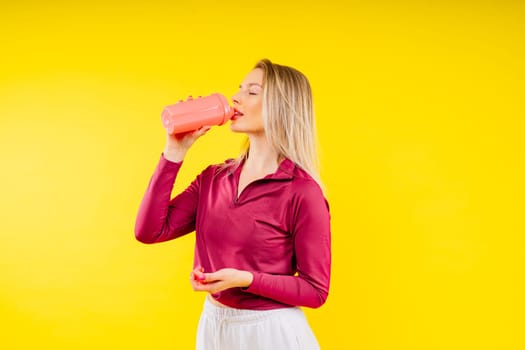 Happy beautiful brunette woman with water bottle or proteine shake on a yellow background