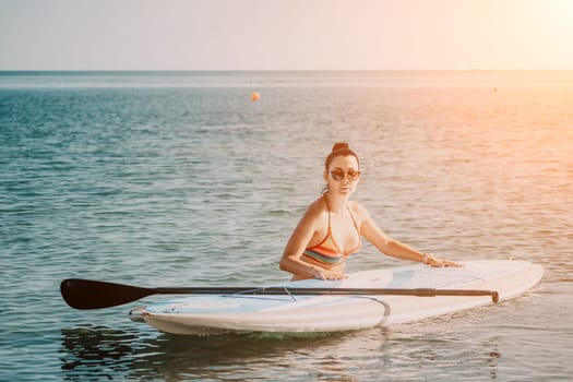 Sea woman sup. Silhouette of happy middle aged woman in rainbow bikini, surfing on SUP board, confident paddling through water surface. Idyllic sunset. Active lifestyle at sea or river