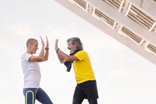 senior sports man and his personal trainer smiling happily high five with joy after a training session, concept of active and healthy lifestyle in the middle age, copy space for text