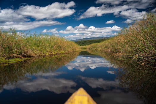 A kayak glides through a serene waterway under a bright, cloud-streaked blue sky.