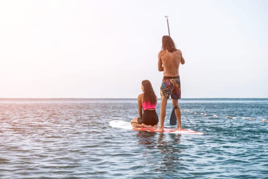 Sea woman and man on sup. Silhouette of happy young woman and man, surfing on SUP board, confident paddling through water surface. Idyllic sunset. Active lifestyle at sea or river