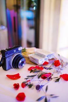 Fujifilm Instax camera lies on the table near flowers and cartridges. High quality photo