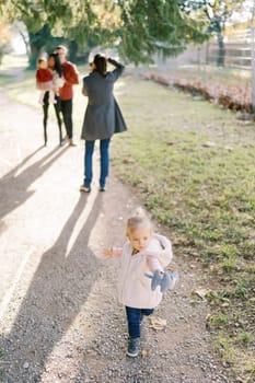 Little girl is standing on a path against the background of a photographer taking pictures of a married couple with a child. High quality photo