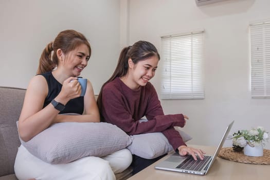 Two women communicate with friends and classmates via video link using laptop and smartphone in living room. Friends, friendship, time together..