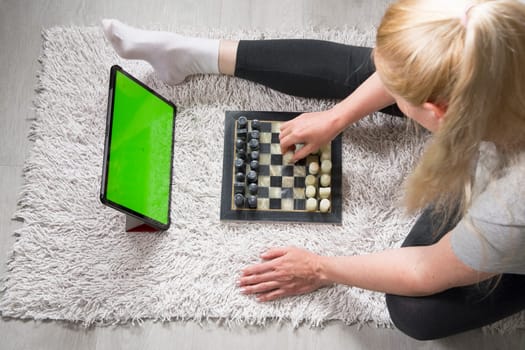 woman playing chess on the carpet with a virtual partner on a tablet, green screen tablet, mockup for app advertising, online remote games, high quality photo