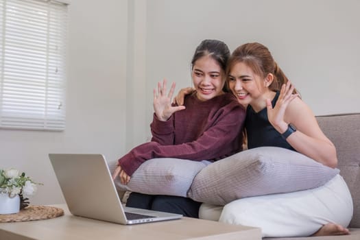 Two women communicate with friends and classmates via video link using laptop and smartphone in living room. Friends, friendship, time together..