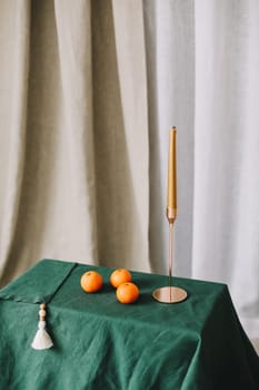 Stylish home decor in rustic style. Table with a golden candle in candlestick, green tablecloth, tangerines. Festive Cozy room decorated for Christmas or New year