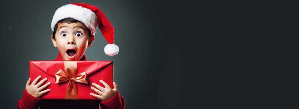 Surprised little boy in Santa Claus hat holding gift box. Christmas holidays. Boxing Day shopping. Holiday shopping.