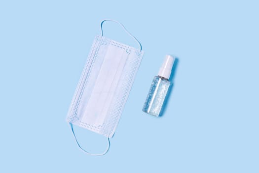 Flat lay with a medical mask placed in the center, a bottle of antiseptic soap or hand sanitizer.