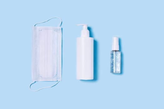 Flat lay with a medical mask placed in the center, a bottle of antiseptic soap and a hand sanitizer.