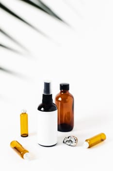 Two glass spray bottles on white background surrounded by crystal of quartz, the vials and herbs.