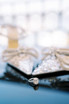 Engagement ring lies on the mirror table near the bride shoes. High quality photo