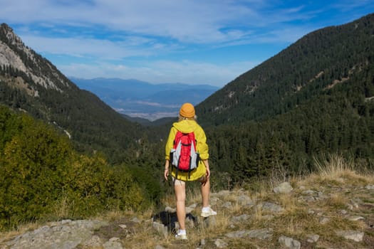 A girl on top of a mountain with green grass looks at a beautiful mountain valley. Landscape with a sporty young woman in a yellow raincoat. Travel and tourism. Hiking.