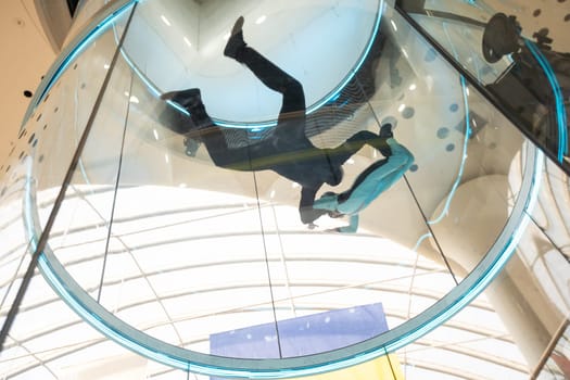 Excited teenage girl in helmet flying in aerodynamic tube wind tunnel. Skydiving training. High quality photo