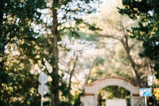 White drone flies through the park near the brick gate. High quality photo