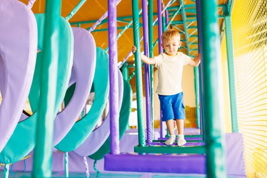 Cute little boy crawling and playing on colorful playground at indoor amusement park
