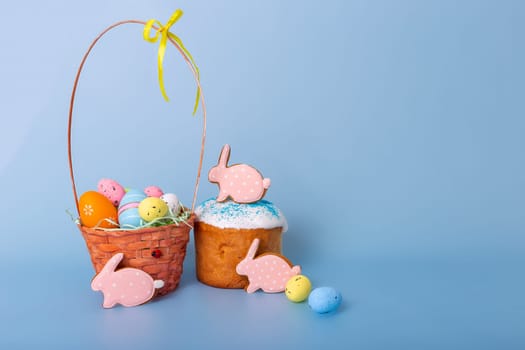 Tasty pink gingerbread in the form of a rabbit , an Easter cake and a basket with decorative multicolored eggs stand on a blue background.