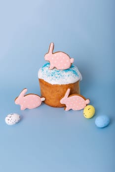 Three cute pink gingerbreads in the form of a rabbit on Easter cake, decorative eggs, stand on a blue background.