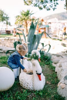Little girl leaned over a flower pot in the shape of a swan in a flower bed. High quality photo