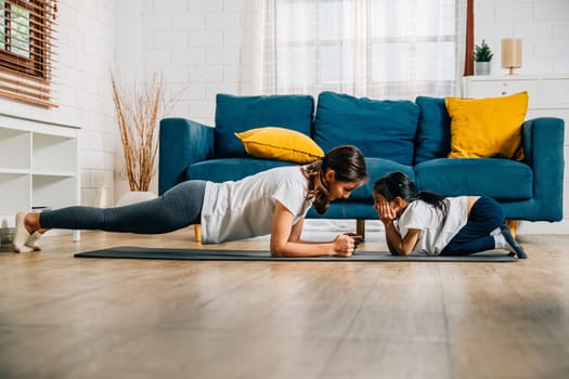 A beautiful young woman and her charming daughter share smiles during their family yoga finding harmony and togetherness while stretching and balancing at home.