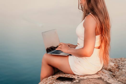 Freelance women sea working on the computer. Good looking middle aged woman typing on a laptop keyboard outdoors with a beautiful sea view. The concept of remote work