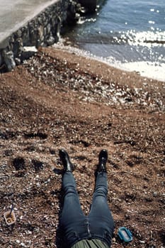 Women legs in jeans and high boots lie on a pebbly beach by the sea. Cropped. Faceless. High quality photo