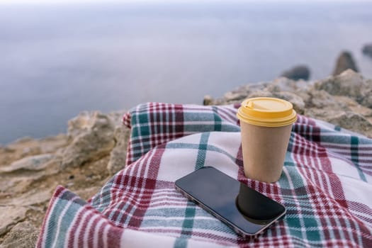 Laptop coffee on blanket with ocean view. Illustrating serene outdoor laptop use. Freelancer enjoying their time outdoors while working or browsing the internet
