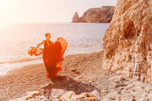 Woman red dress sea. Female dancer in a long red dress posing on a beach with rocks on sunny day. Girl on the nature on blue sky background