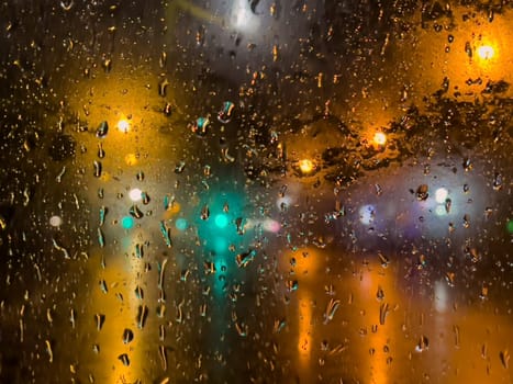 Rain bokeh road lights. Abstract shot of evening city traffic bokeh. Multicolored lights of the evening city and passing cars through a wet rainy window