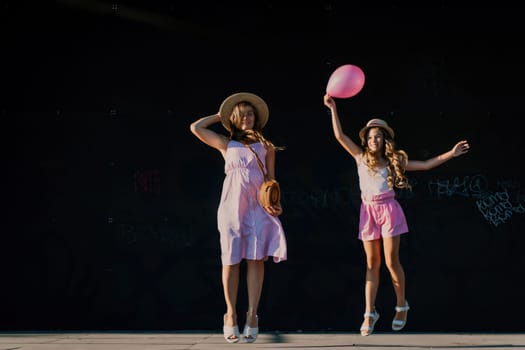 mother and daughter jumping in pink dresses with loose long hair on a black background. Enjoy communicating with each other.