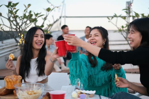 Cheerful male and female friends enjoying happy hour at terrace party and toasting drinks